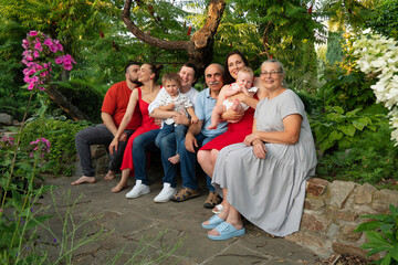 Family shares a tender moment sitting closely together on a bench in a flourishing garden, expressing love, warmth, and happiness on a sunny summer day. Three generations. A close-knit family