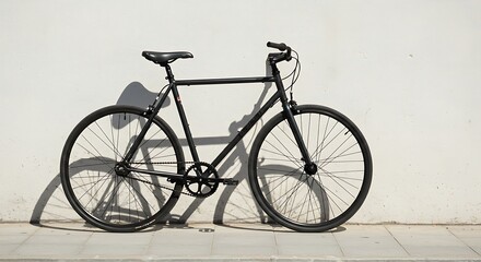 Fototapeta premium A minimalist black single-speed bicycle parked against a textured white urban wall, casting a distinct shadow in the bright sunlight.