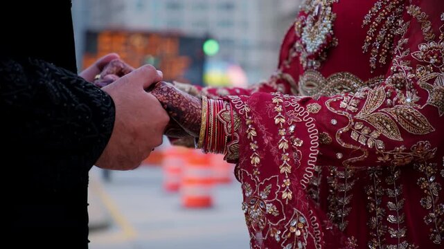 Groom is holding brides hands in Traditional henna painting in the downtown of the big city. Red color is the traditional Indian clothes, Elements of hindu wedding. 