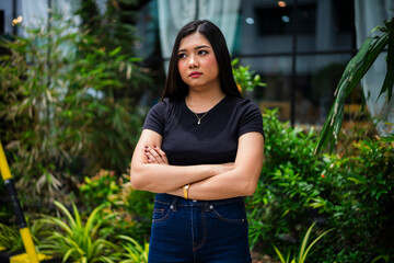 A sulking young Asian woman standing with her arms crossed, wearing a disappointed and sad...