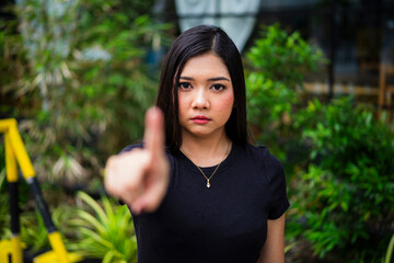 A serious young Asian woman pointing one finger upward close to the camera with a firm and...