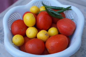 red tomatoes , green chilly and lemon in a blue basket