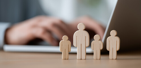 Wooden human silhouettes stand in front of blurred person typing on laptop.