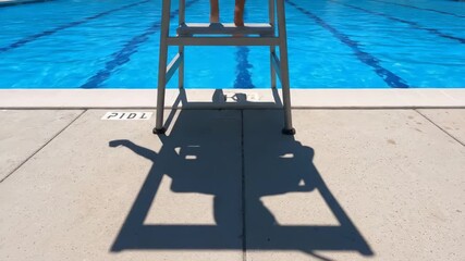 Lifeguard Shadow at Poolside - The shadow of a lifeguard is cast on the concrete deck beside a bright blue swimming pool. The lifeguard sits perched on a high chair overlooking the water. - Powered by Adobe