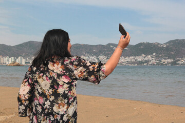 A 40-year-old Latina woman takes selfies alone and calmly while walking along the beach during her...