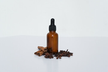 Brown dropper bottle with cinnamon sticks, cloves, and star anise on white background