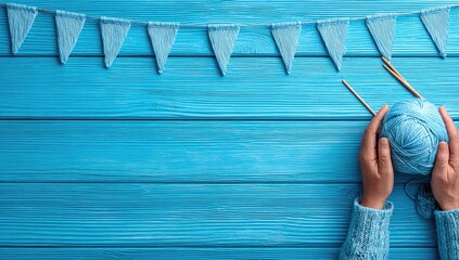 Hands holding a ball of blue yarn on a blue wooden surface with decorative flags