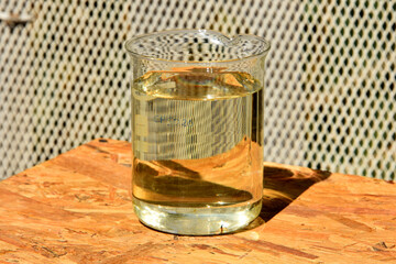 Treated Water in a Glass Beaker. A clear, yellowish liquid, representing treated water, is contained within a glass beaker on a wooden surface

