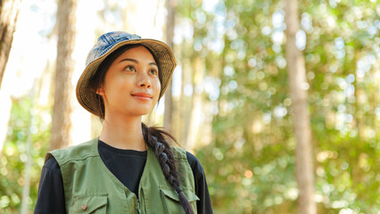 A woman wearing a green vest and hat is looking at the camera. She has long hair. The hat is blue and white