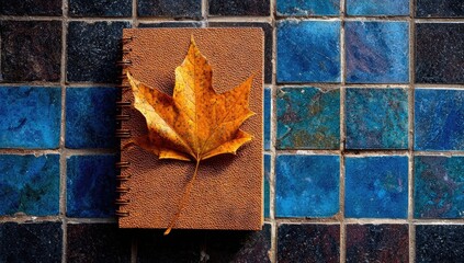 Autumnal notebook with dried leaf on patterned tiles