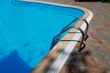 Close up grab bars ladder in the blue swimming pool outdoors