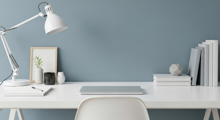 Minimalist modern workspace with closed laptop, stylish lamp, framed artwork, succulent plant, and organized books on sleek white desk against blue wall