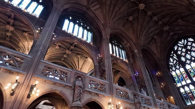 Interior view of the historic John Rylands Library in Manchester, showcasing its stunning architecture with high arches, a ribbed vault ceiling, stained glass windows, and a statue