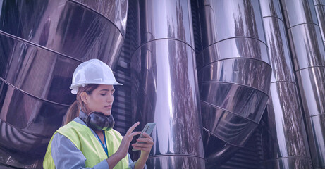 Female engineer wearing safety helmet and vest, using smartphone and inspecting industrial air...