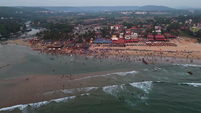 Drone flying around the Baga beach full of people, sunny evening in Goa, India