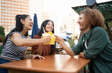Happy multiethnic friends are toasting and laughing together while enjoying fruity drinks at an...