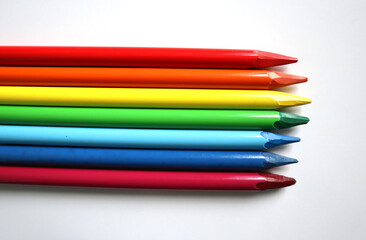 Photo of colored pencils arranged in the colors of the rainbow on white background. Pencils without wood. Pencils are placed in the middle, horizontally. Go beyond the background on the left side.