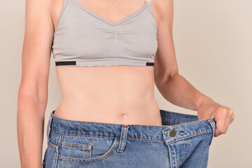Slim mature woman wearing oversize jeans on the pale brown background. Body fit, dieting and weight...