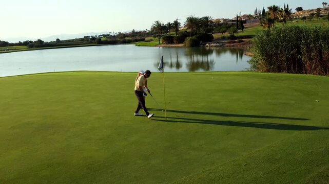 Golfers putting on green near lake in resort