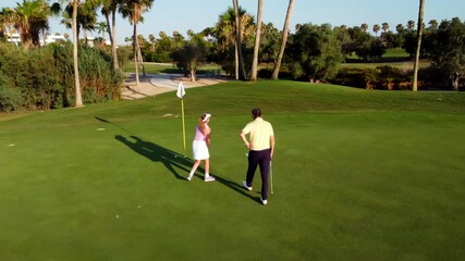 Golf instructor coaching female golfer on putting green