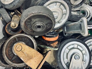  A close-up, top-down view of a pile of old, greasy caster wheels and metal mounts. The various sizes and worn condition suggest they are scrap or used parts from industrial carts and equipment.