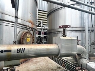 A close-up view of large industrial tanks and pipes, highlighting the intricate connections and a warning sign, symbolizing the powerful and complex systems of a factory or refinery.