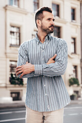 Fototapeta premium Portrait of handsome confident stylish hipster lambersexual model. Sexy modern man dressed in blue shirt and trousers. Fashion male posing on street background in Europe city at sunset