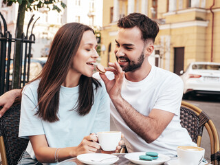 Smiling beautiful woman and her handsome boyfriend. Happy cheerful family. Couple drinking coffee in restaurant. They drinking tea at cafe in the street. Holding cup. Feeding his girlfriend