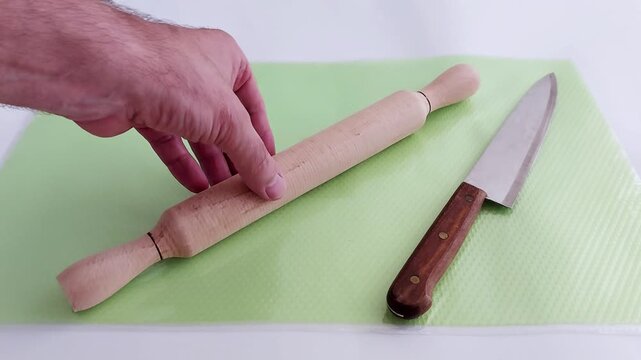 A wooden rolling pin rests beside a kitchen knife on a soft green mat-minimalist kitchen tools arranged with quiet precision, ready for a simple culinary task