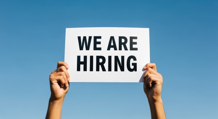Recruitment Announcement: Hands Holding "We Are Hiring" Sign Against a Bright Blue Sky, Seeking Job Applicants