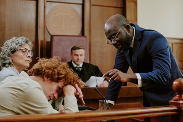 Black middle aged man in suit addressing Caucasian teenager with head down while middle aged...