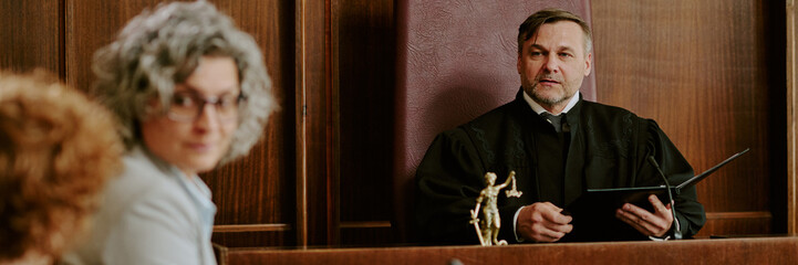Caucasian middle aged man judge holding folder presiding over courtroom session with two women in...
