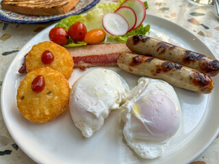 Two poached eggs served with hash brown, pork sausages and bacon