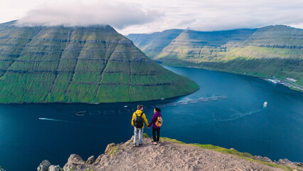 Breathtaking view of hikers overlooking the stunning landscape of Faroe Islands at sunrise