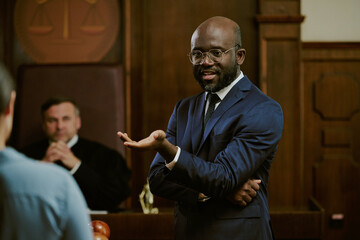 Black middle aged man standing in courtroom gesturing while speaking to unseen , judge sitting in...