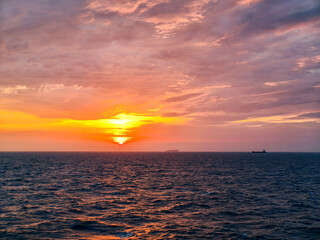 A vivid sunset over an expansive ocean, with deep orange and yellow hues blending into a purple sky. 