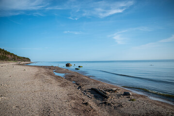 Sandy beach with scattered rocks and driftwood stretches along a tranquil coastline. 