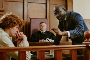 Black middle aged man in suit gesturing while addressing Caucasian teenage boy sitting at witness...