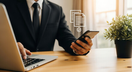 A businessman in a suit using a laptop and a smartphone with document approval icon overlayed on the screen