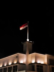 Indonesian National Flag Flying at Night on Top of Illuminated Building – Red and White Banner...