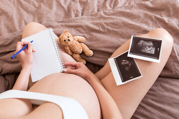 Top view caring future mother writing diary with ultrasound. pregnant woman tummy making notes...
