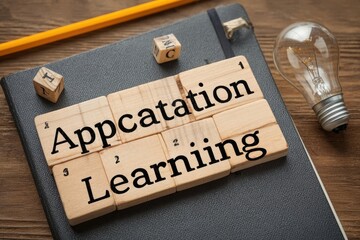 Wooden blocks spelling out "Appication Learning" on a dark notebook, with a pencil and lightbulb
