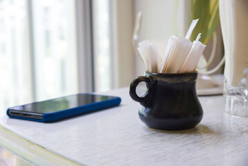 A mug with a toothpicks in a package inside it is placed on a table next to a cell phone. The mug...