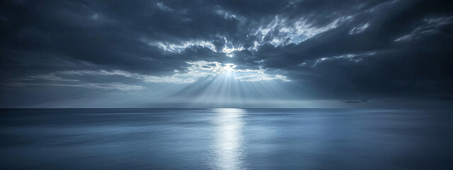 Panoramic landscape of calm ocean with dramatic stormy sky and golden sun rays breaking through clouds above water