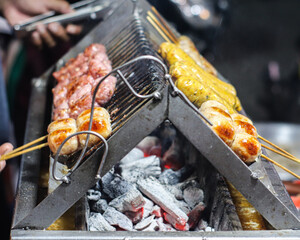 Grilled Thai sausages, sour pork, and spicy sausage skewers on a charcoal grill at night, glowing...