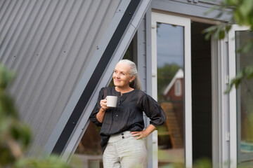 portrait of a cheerful elderly woman with a cup of tea in the garden about her home. concept...