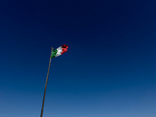 Italian flag waving in a strong wind against a blue sky