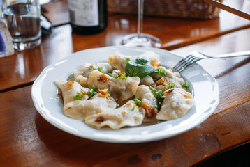 Plate of pierogi topped with caramelized onions and herbs served on a rustic wooden table with wine in background. Locally sourced ingredients, farm-fresh food, sustainable dining, countryside cuisine