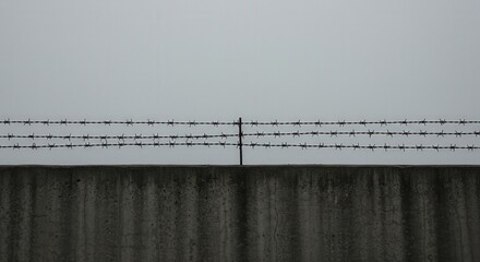 Concrete wall with barbed wire on top, minimalist security barrier on gray background, strong protective element, industrial fencing, basic protective infrastructure