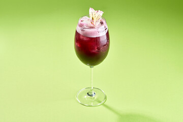 A refreshing cocktail with a flower garnish, served in a stemmed glass on a bright green background.